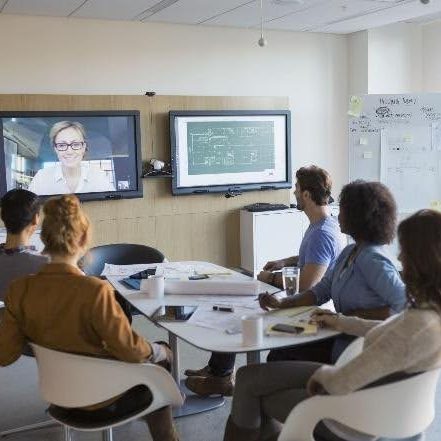 A group of adults seated at a table looking at another adult on a screen at the front of the room